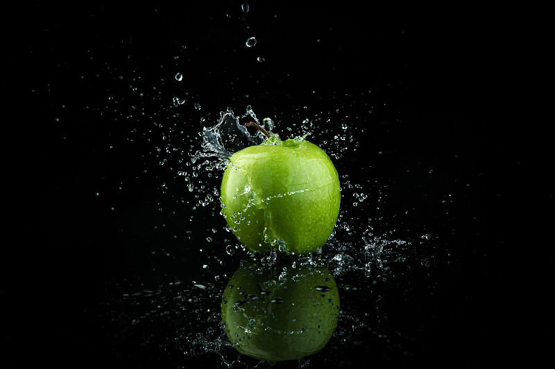 青苹果落在水中，溅起黑色背景。图片下载