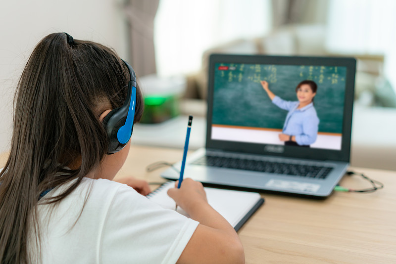 亚洲女学生视频会议电子学习与教师在家里的客厅电脑。家庭教育和远程教育、在线教育和互联网保护免受COVID-19病毒的感染。图片素材