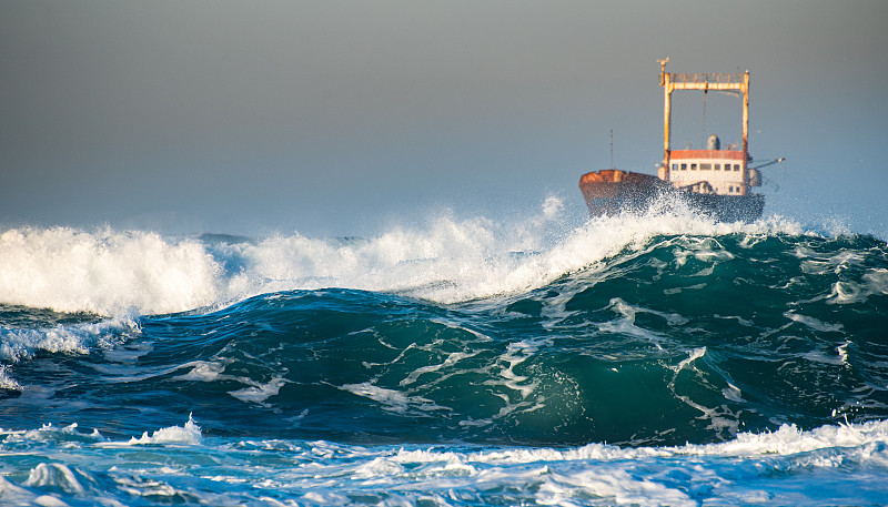 被遗弃的船在暴风雨的海上和大风浪在日落。图片素材