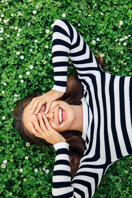 高角度的微笑年轻女子躺在草地上图片素材