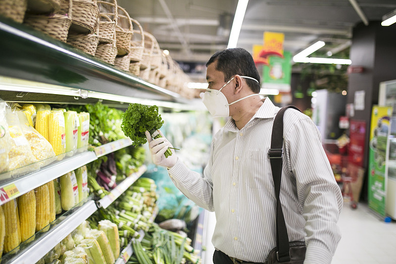 一名亚洲行政人员在超市买绿色食品，戴着医用防护口罩图片下载