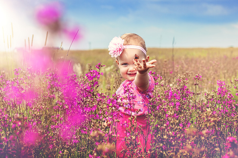 一个小女孩在一片粉红色的花丛中，手里拿着一只蝴蝶。图片素材