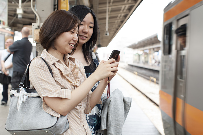两个20多岁的女孩在地铁上用手机图片下载