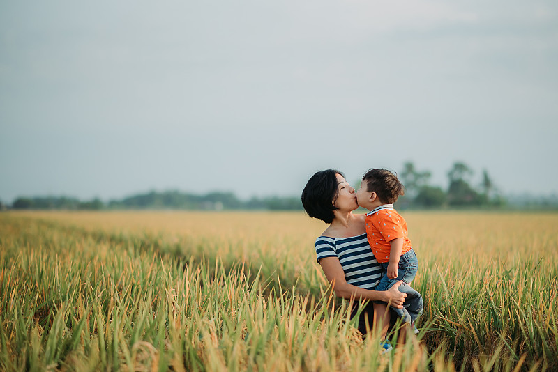 亚洲华人母亲抱着她的儿子在稻田里亲吻他图片素材