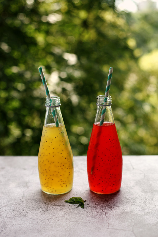 玻璃瓶与夏季饮料超级食物草莓和菠萝汁与种子在绿树的背景。垂直的照片。摄影图片下载