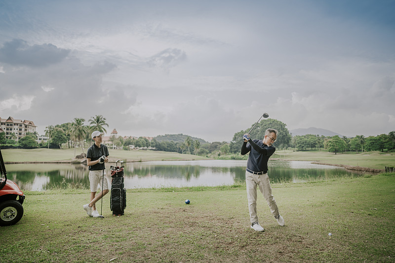 周末，一个成熟的亚洲华人在高尔夫球场挥杆，他的儿子在一旁观看图片下载