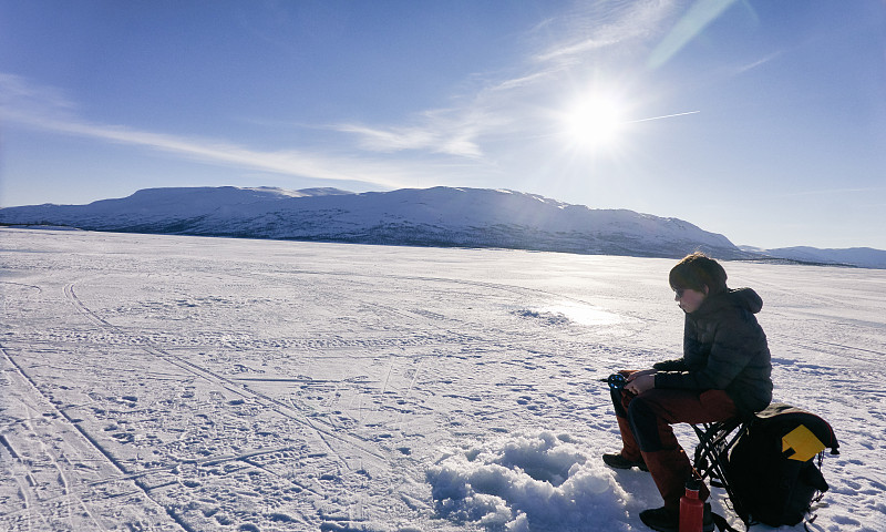 Boy ice-fishing on frozen lake in Vasterbottens Lan, Sweden.图片素材