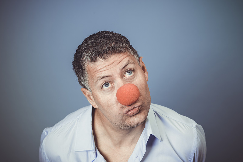 中年男子蓝色衬衫和红色小丑鼻子在蓝色背景下摆姿势图片下载