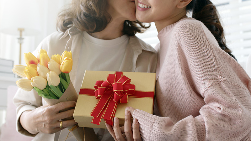 迷人美丽的亚洲中年妈妈与成年的女儿坐在一起赠送礼盒和鲜花在家庭时刻庆祝母亲节。大喜的关系，愉快的孩子拥抱与退休的妈妈的关系。图片下载
