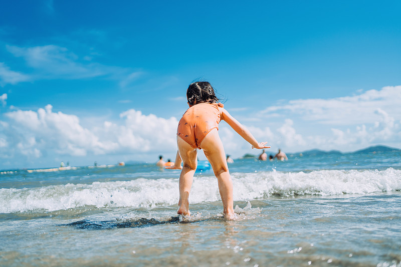 后视图可爱的小亚洲女孩跑和跳在海滩的海浪。在一个阳光明媚的夏日，在海滩上玩得开心图片下载