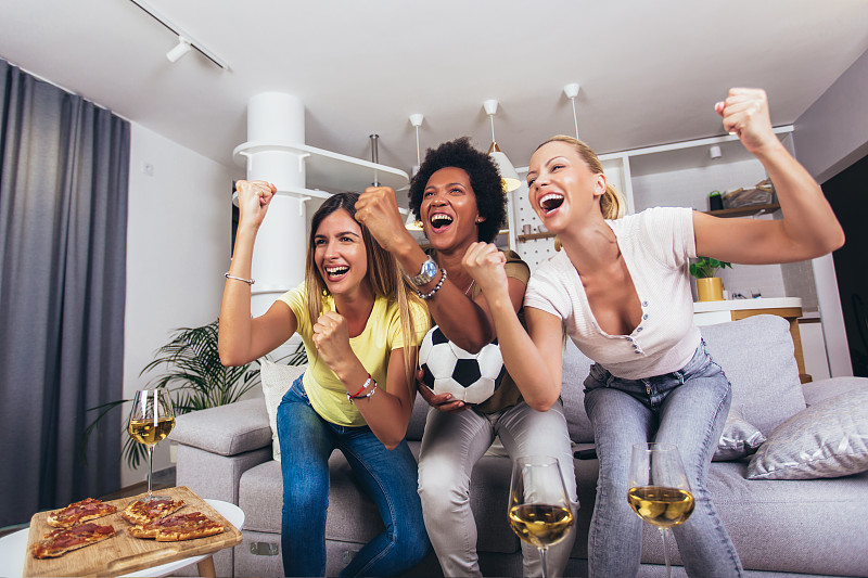 一群兴高采烈的女性朋友在家里观看足球比赛，庆祝胜利。图片下载