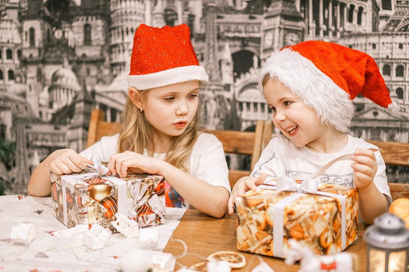 孩子们带着礼物站在圣诞树旁，穿着红色的毛衣和圣诞老人的帽子，在除夕或圣诞节在家图片下载