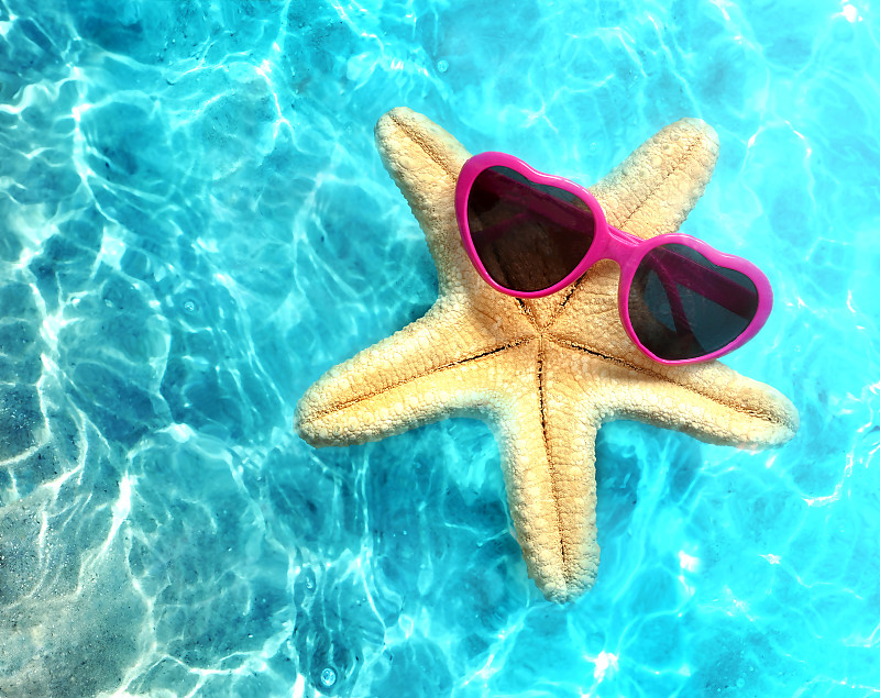 戴着太阳镜的海星在夏天的海水里的海滩上。夏天的背景。图片下载