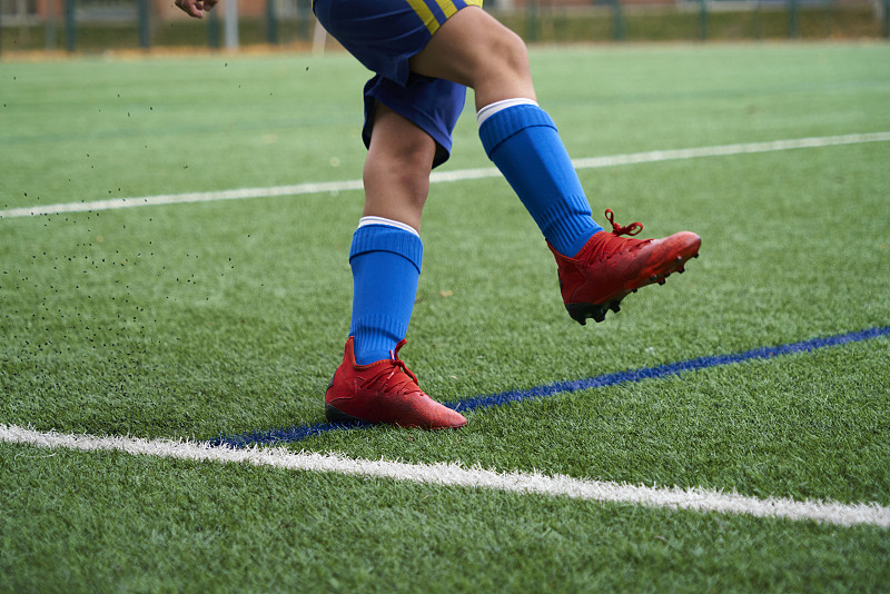 一个穿着足球鞋和运动服的男孩在白天的球场上。概念运动训练，健康生活方式。图片下载
