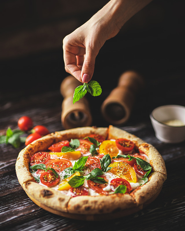 美味的披萨，黑色木制背景，番茄和奶酪。一片有弹性芝士的披萨图片素材