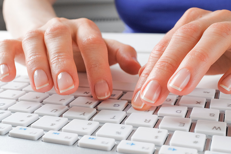 女性用手在电脑或笔记本电脑的键盘上打字。一个女人，坐在办公桌前的办公室职员。商业的概念，自由职业，在家工作。IT支持，网络安全，在线社会支持。网上远程学习。摄影图片