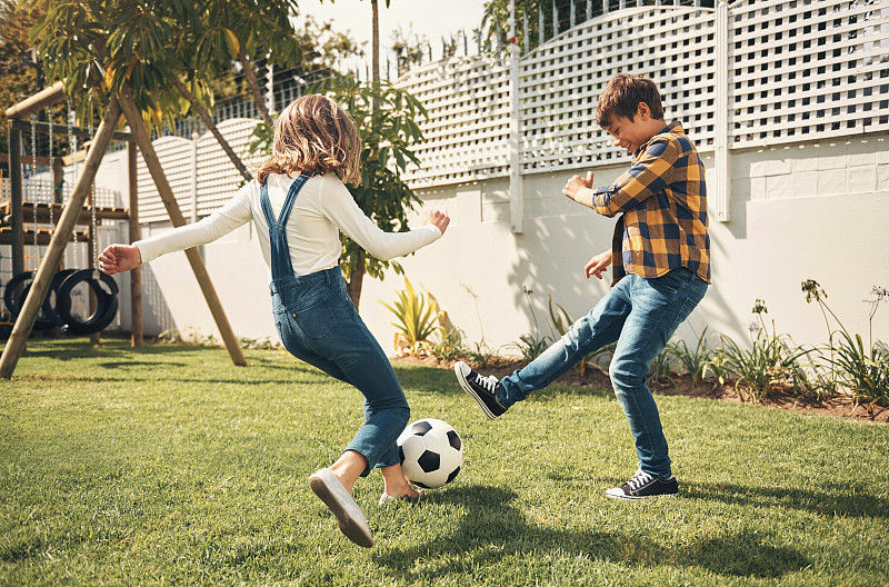 玩耍、游戏和孩子们在花园里进行足球训练，一起在自己家里锻炼健身。年轻，快乐和运动的女孩，男孩或朋友在他们家的后院踢足球图片下载