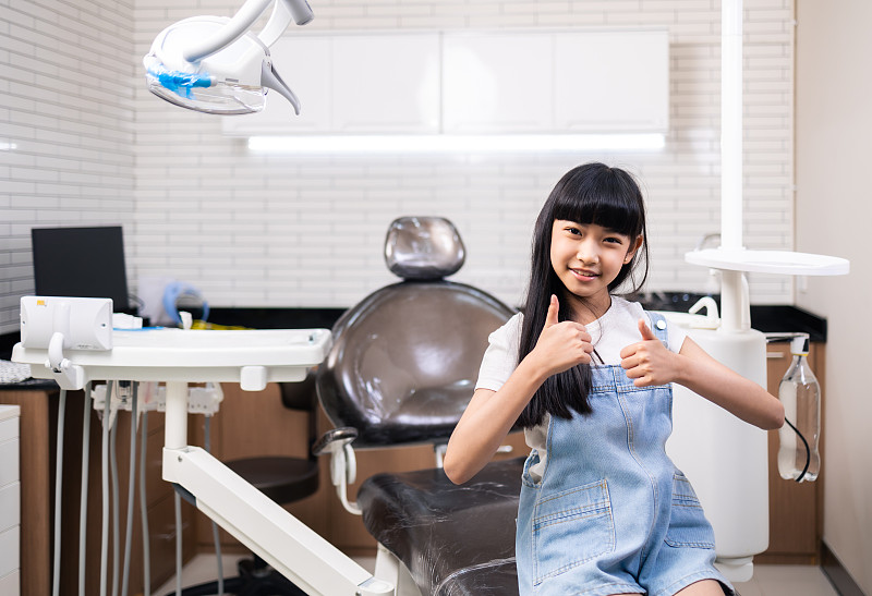 儿童牙科，牙齿健康。特写快乐的亚洲小女孩微笑着看着镜头，坐在牙医的椅子上，接受牙科治疗。图片下载