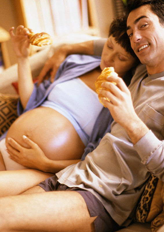 男人和孕妇坐在沙发上吃羊角面包图片下载