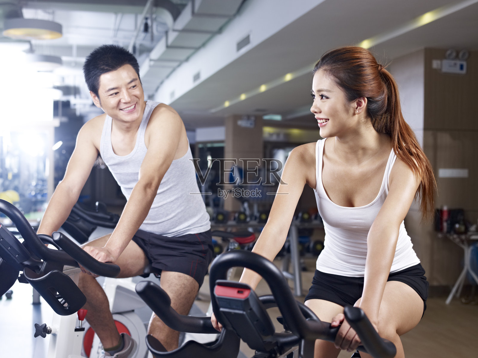穿着白色背心的男人和女人在健身自行车上聊天照片摄影图片