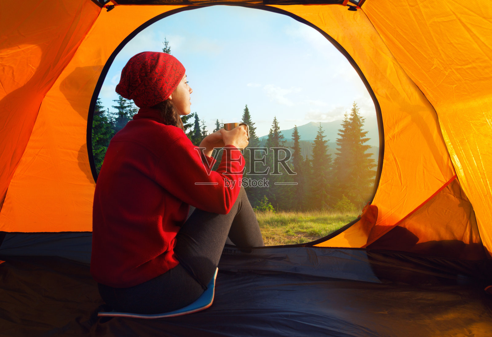 女孩拿着杯子坐在橘黄色的帐篷里看日落照片摄影图片