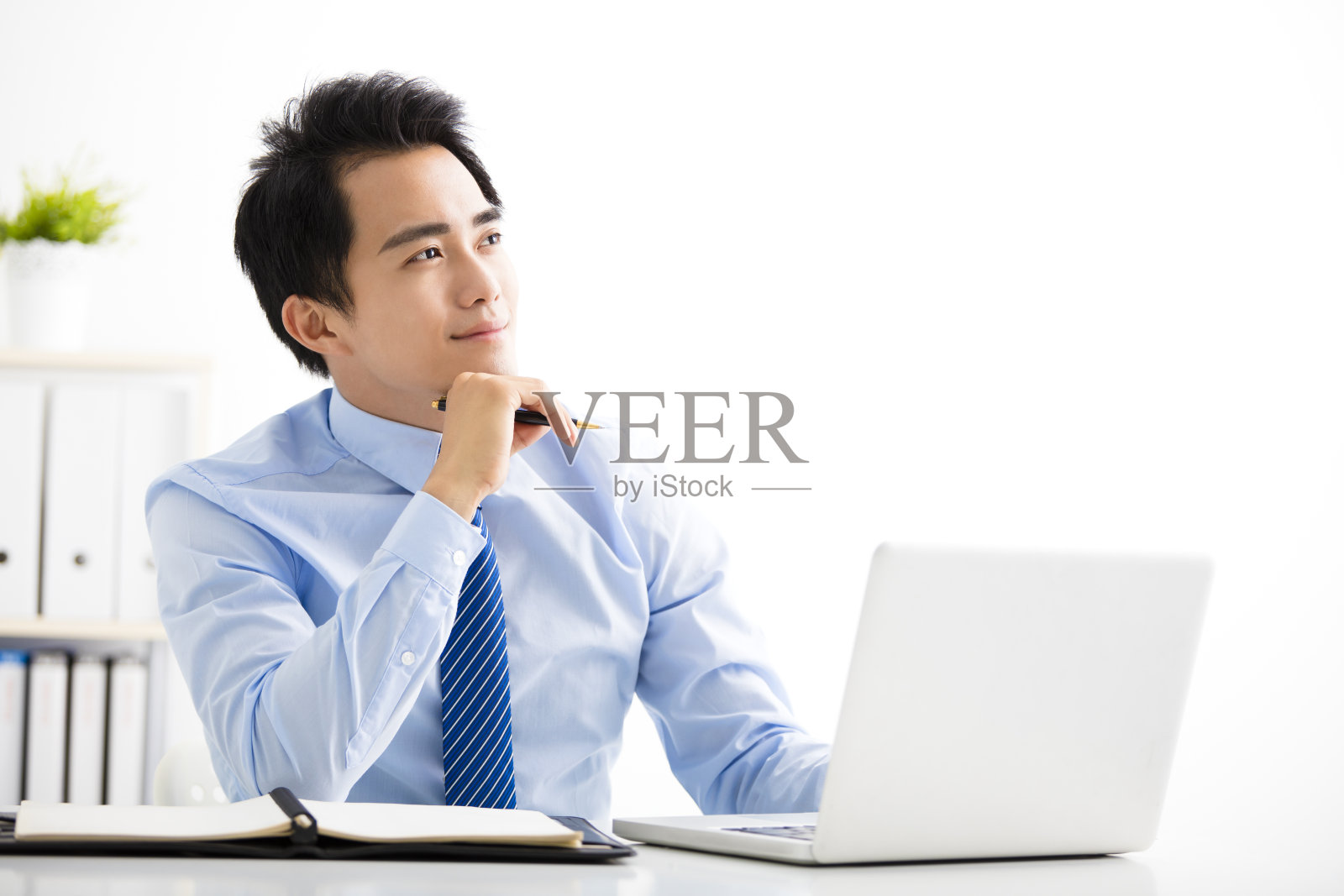 微笑的年轻商人一边用笔记本电脑工作一边思考照片摄影图片