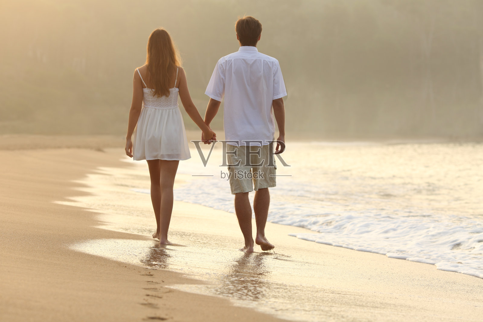 在沙滩上牵手散步的情侣照片摄影图片