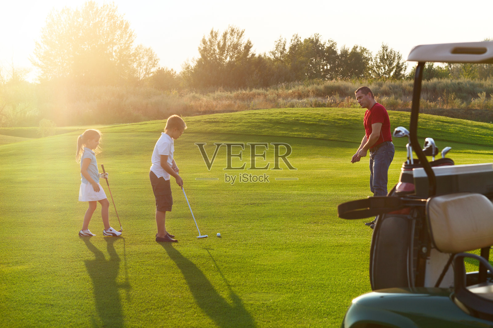 在高尔夫球场上随便玩玩的孩子们。日落照片摄影图片