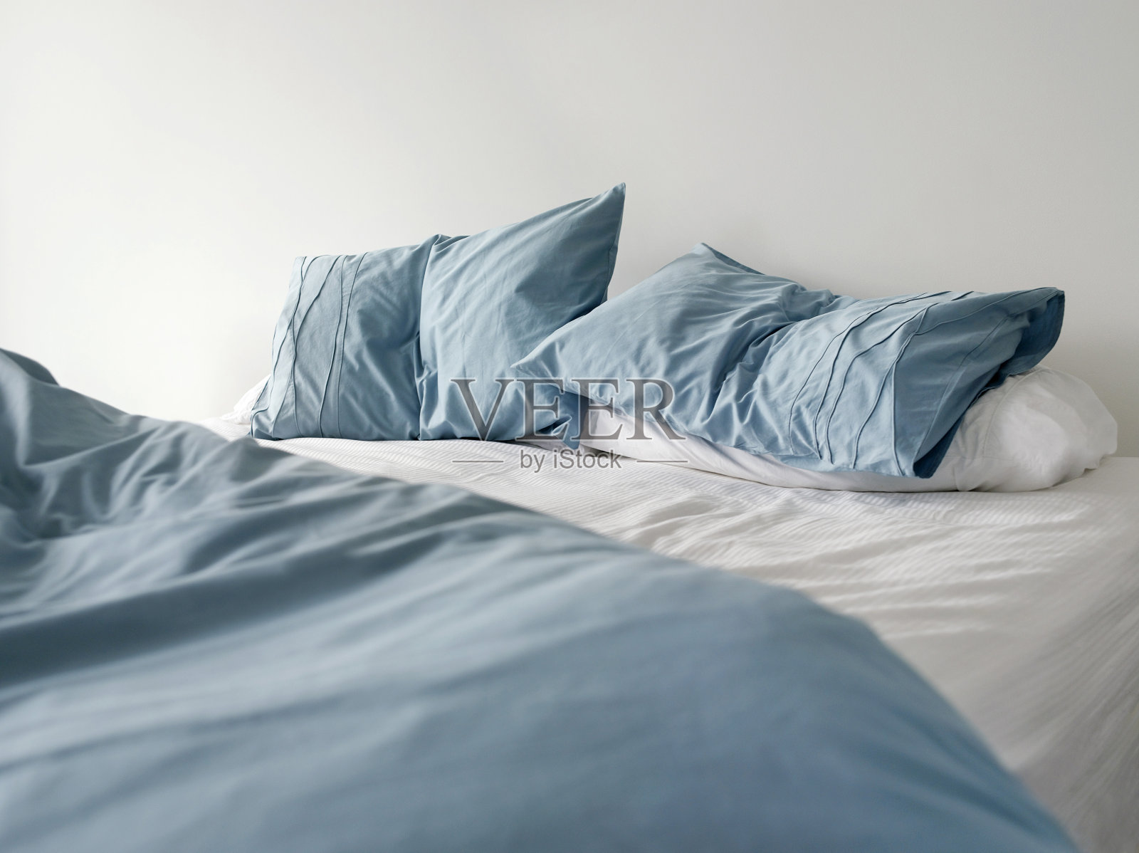 未整理的床，蓝色的亚麻布皱巴巴的照片摄影图片