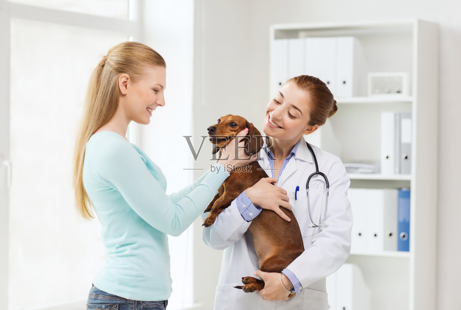 快乐的女人与狗和医生在兽医诊所照片摄影图片