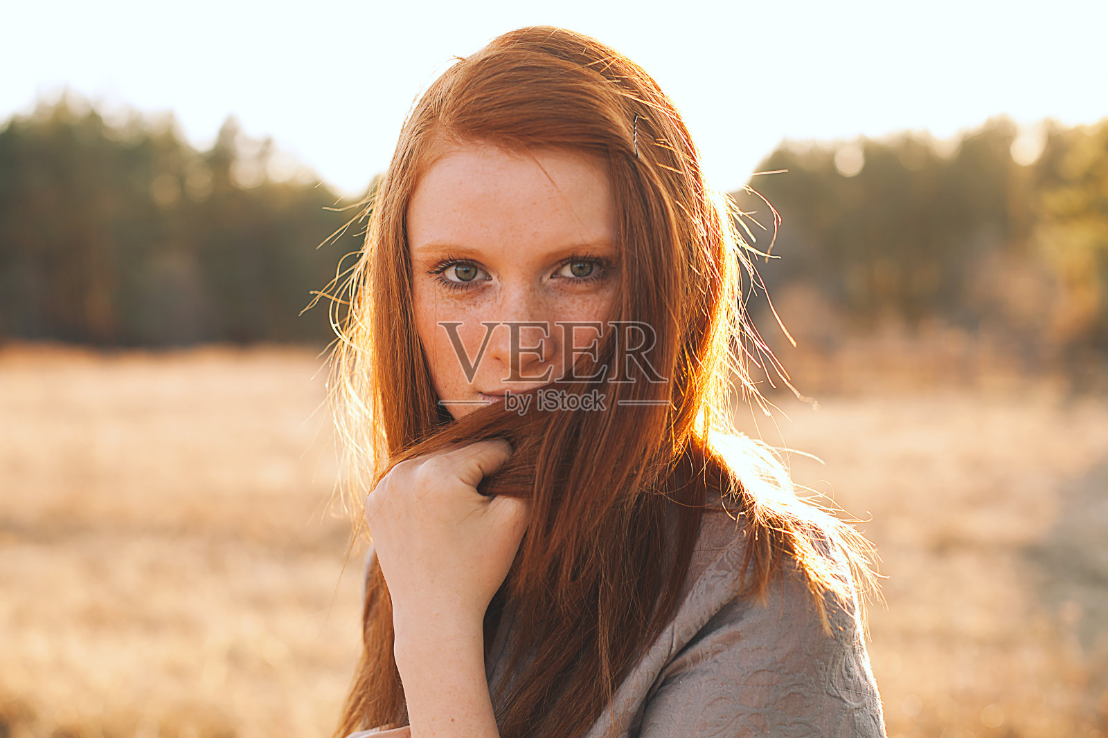 夕阳下金色田野里的红头发年轻女子。照片摄影图片