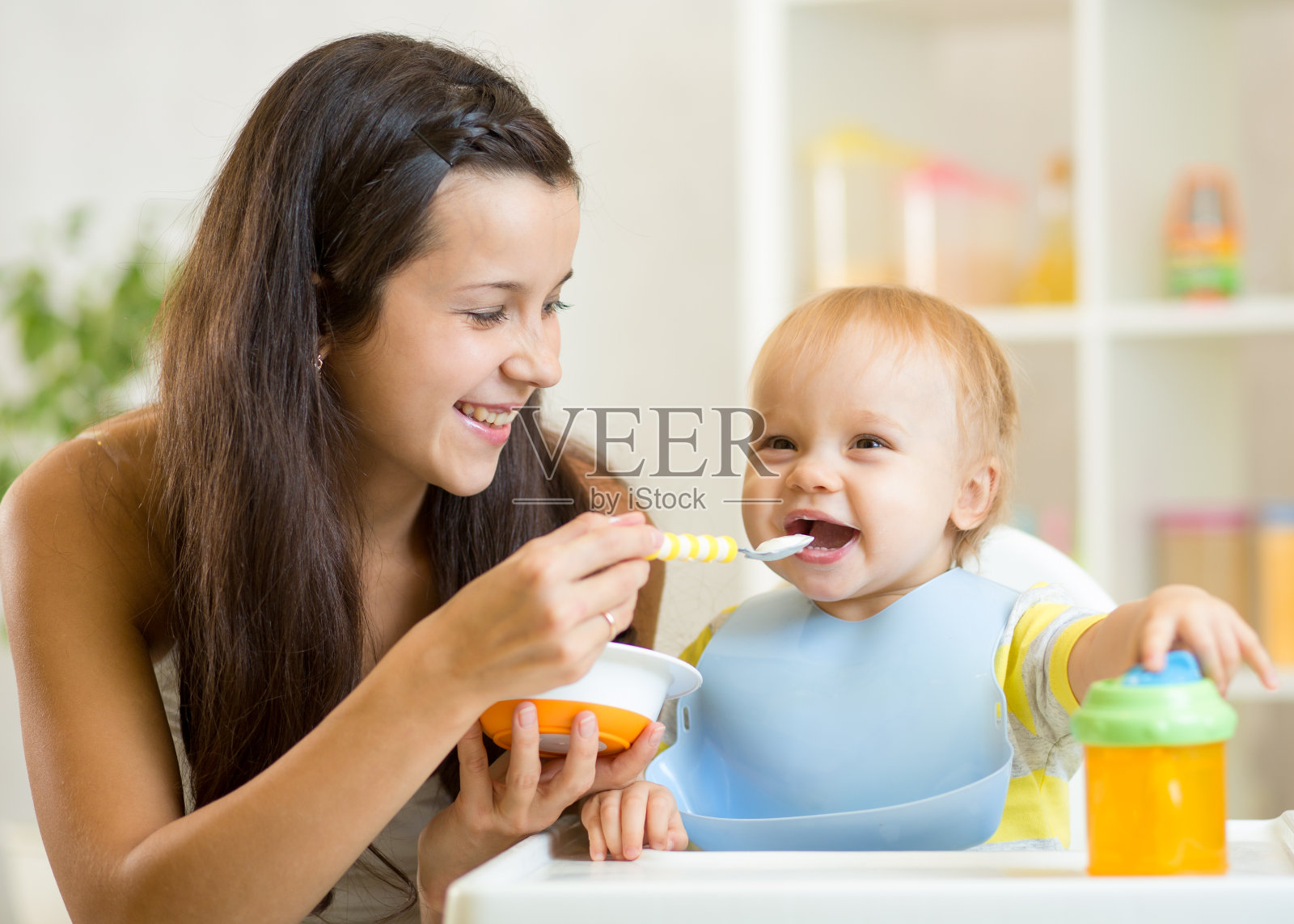 快乐的母亲用勺子喂她的婴儿照片摄影图片
