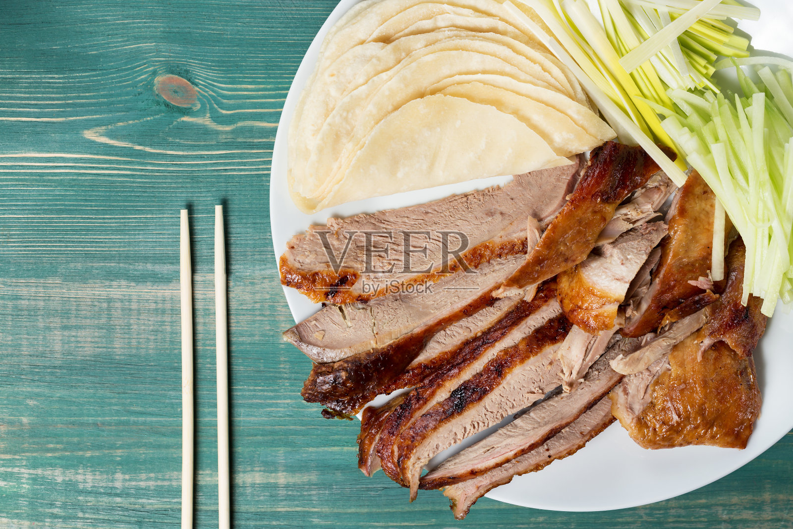 北京烤鸭——中国烤鸭配黄瓜、洋葱和煎饼，放在绿色木桌上，用筷子夹着。俯视图照片摄影图片