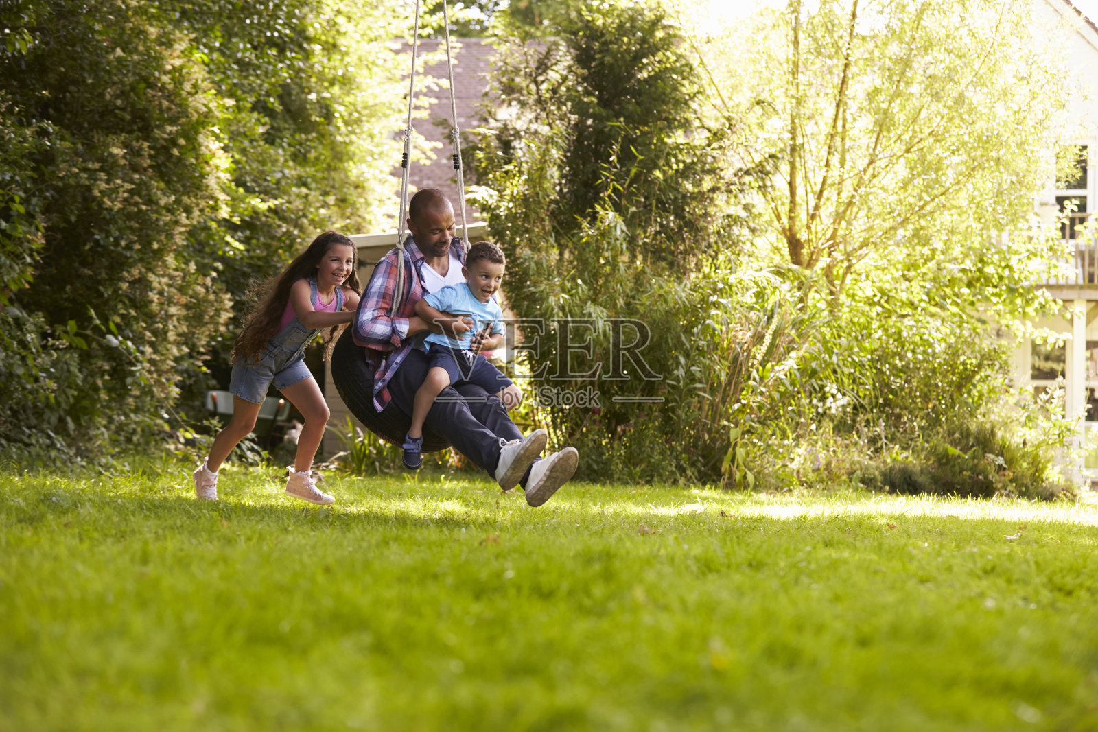 女儿推着父亲和儿子在花园里玩秋千照片摄影图片