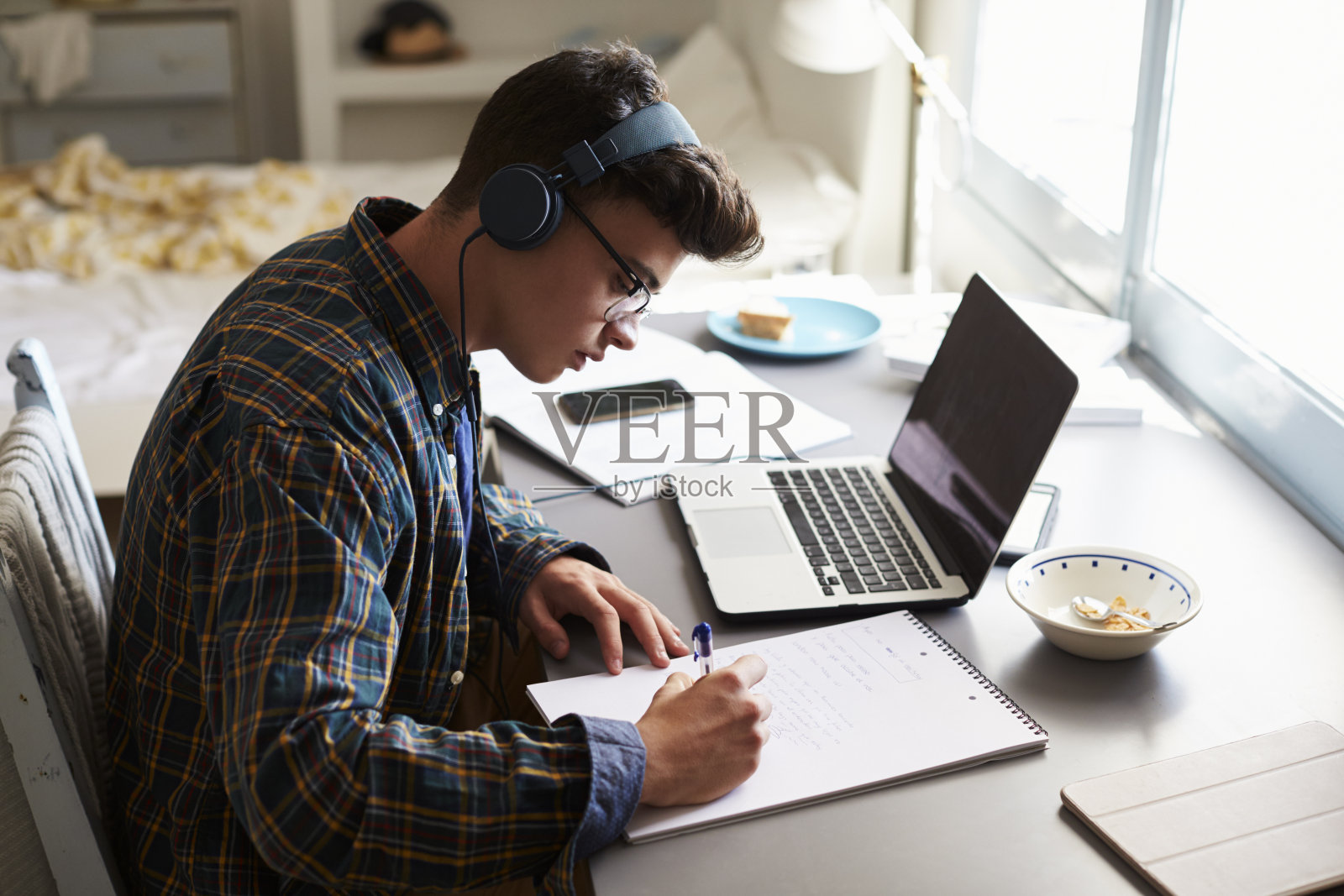 一个十几岁的男孩戴着耳机在卧室的书桌前工作照片摄影图片