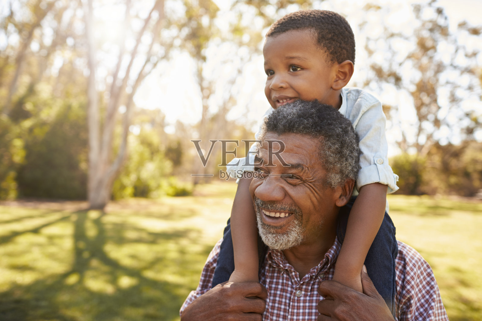 在公园散步时，爷爷把孙子扛在肩上照片摄影图片