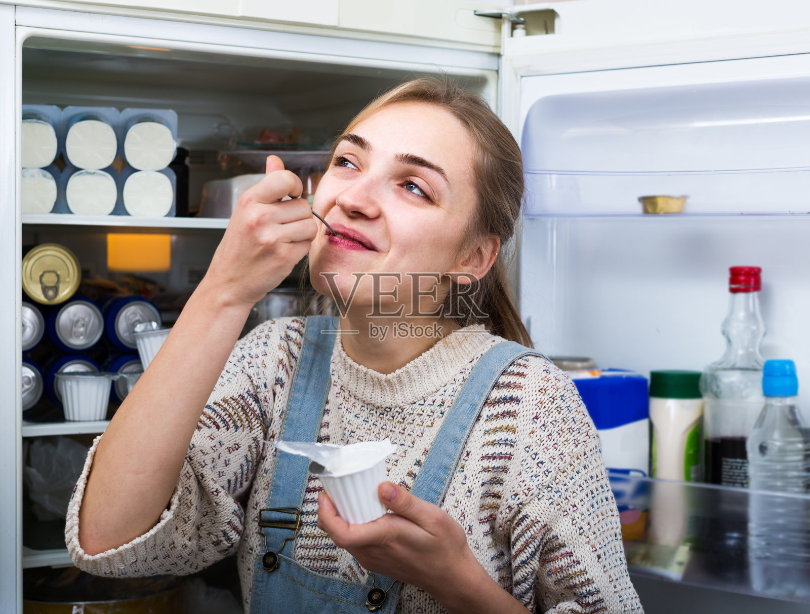 年轻的黑发女子站在冰箱旁边，旁边放着软奶酪照片摄影图片