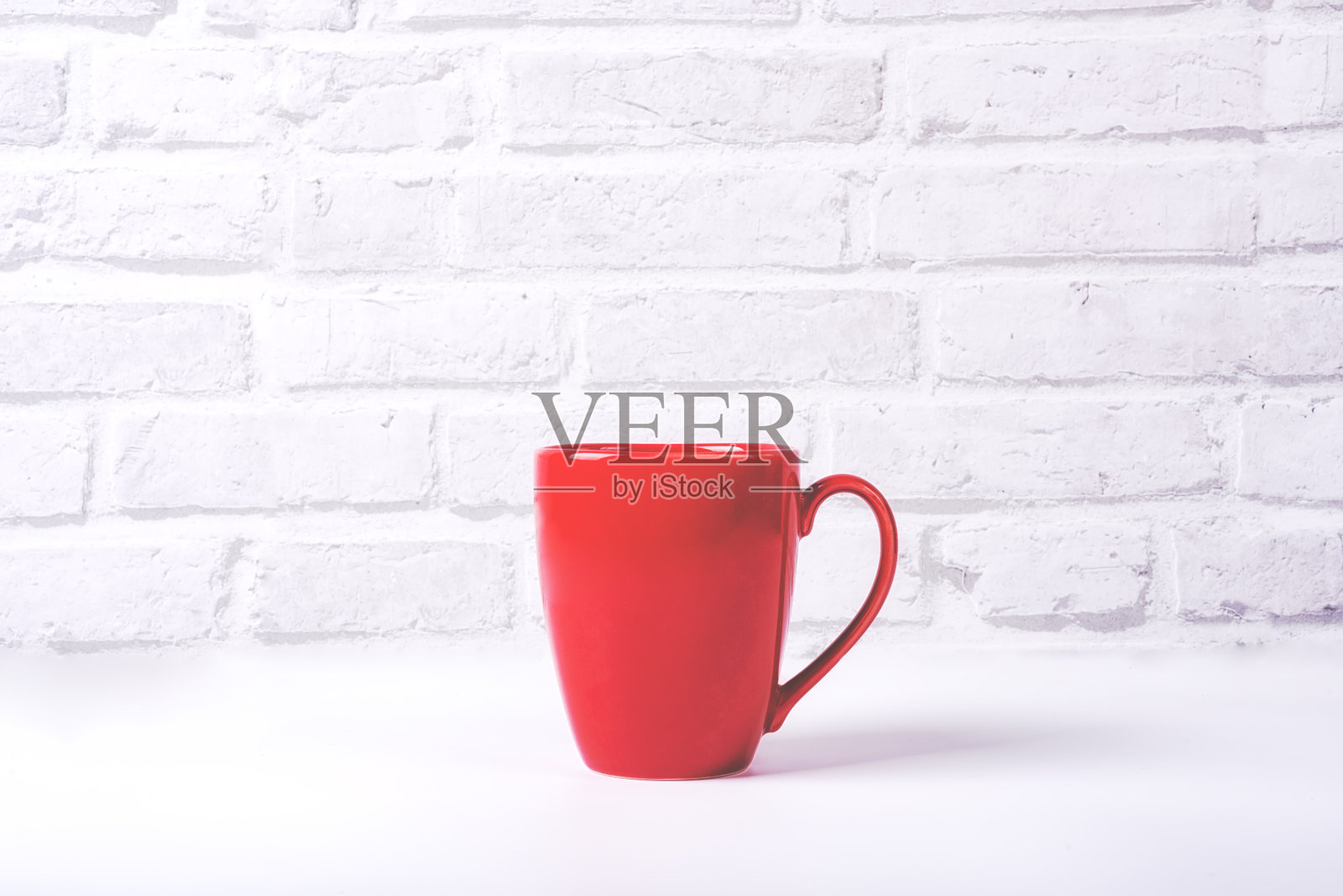 白色的桌子上放着红色的咖啡杯，背景是白砖照片摄影图片