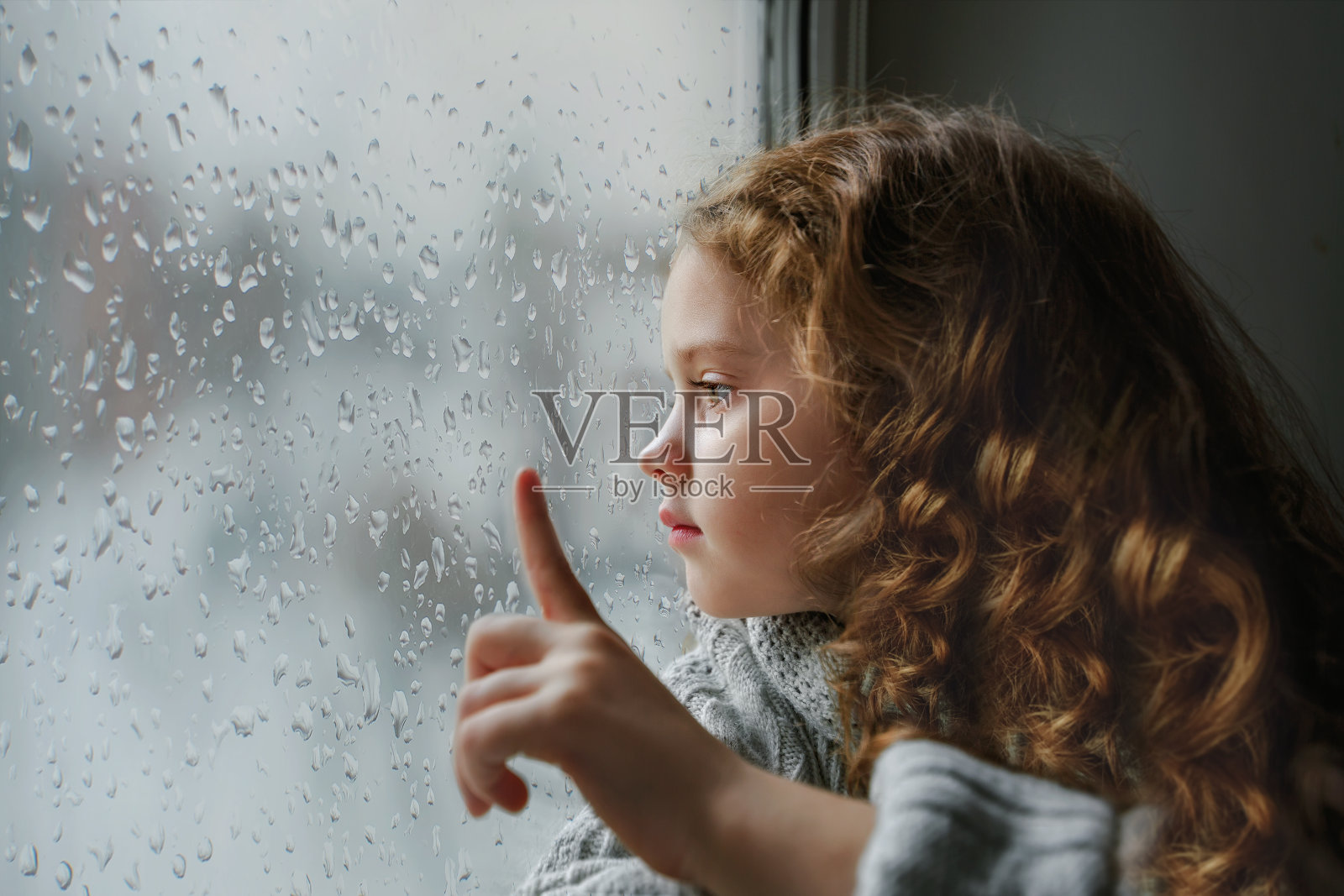 悲伤的小女孩望着窗外。照片摄影图片