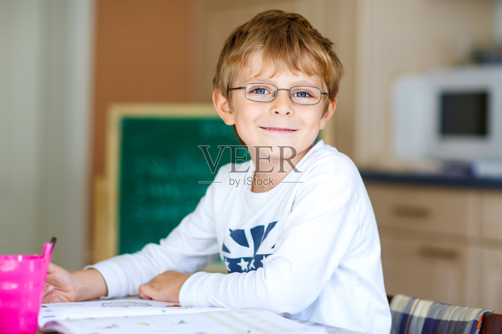 快乐的小学生戴着眼镜在家里做作业照片摄影图片