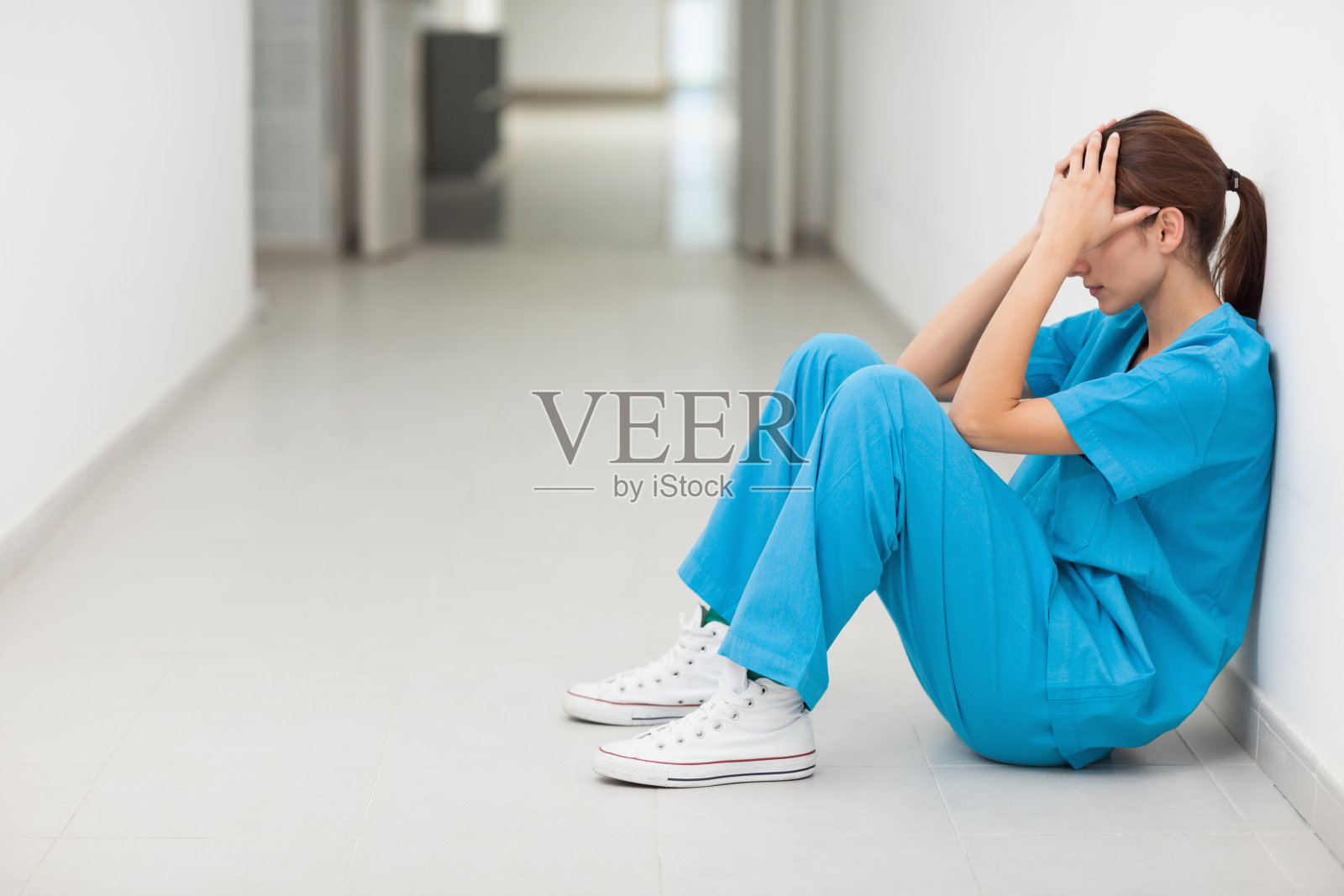 穿着蓝色护士服的女人坐在地板上照片摄影图片