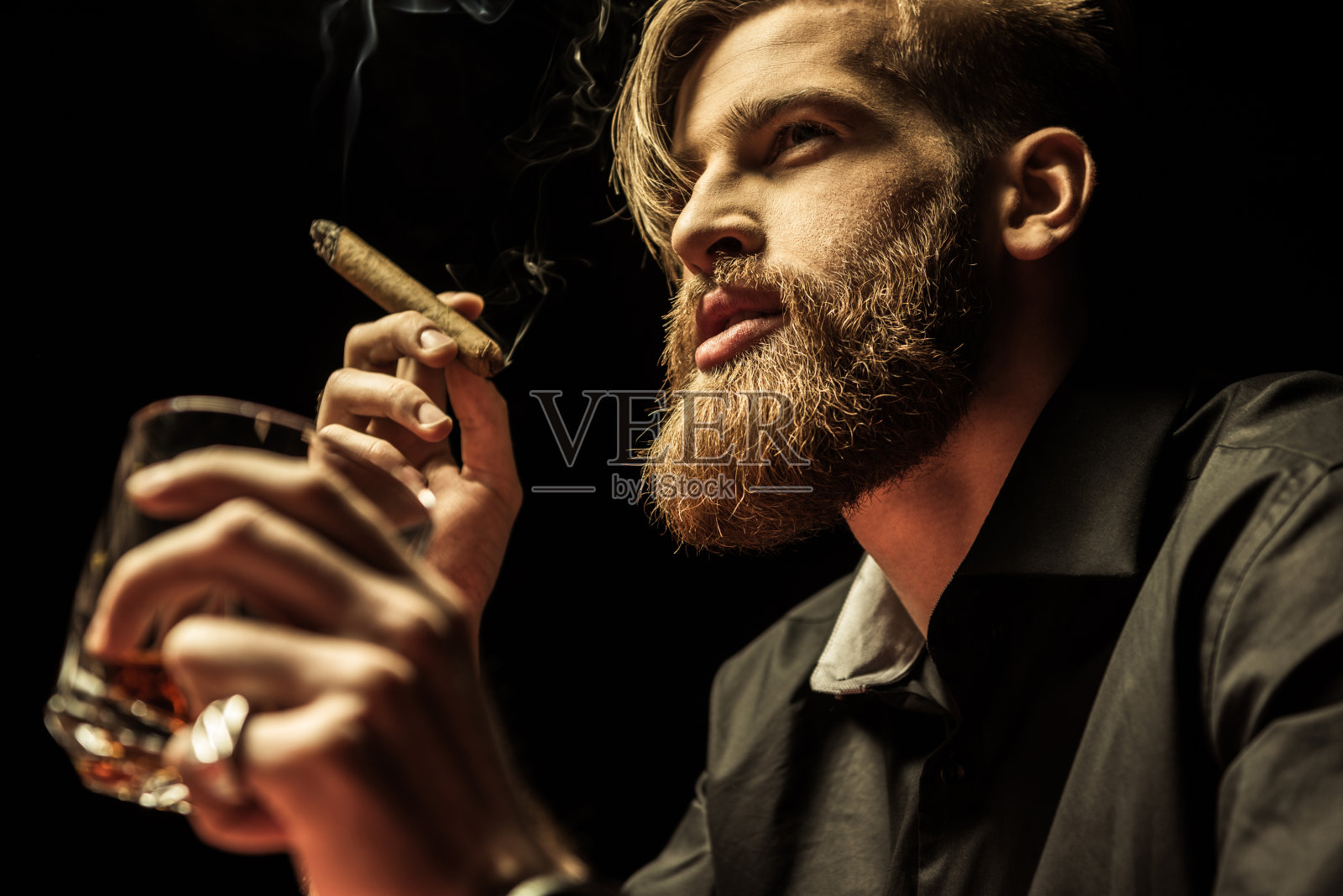 蓄着胡须的英俊男子拿着一杯威士忌，抽烟照片摄影图片