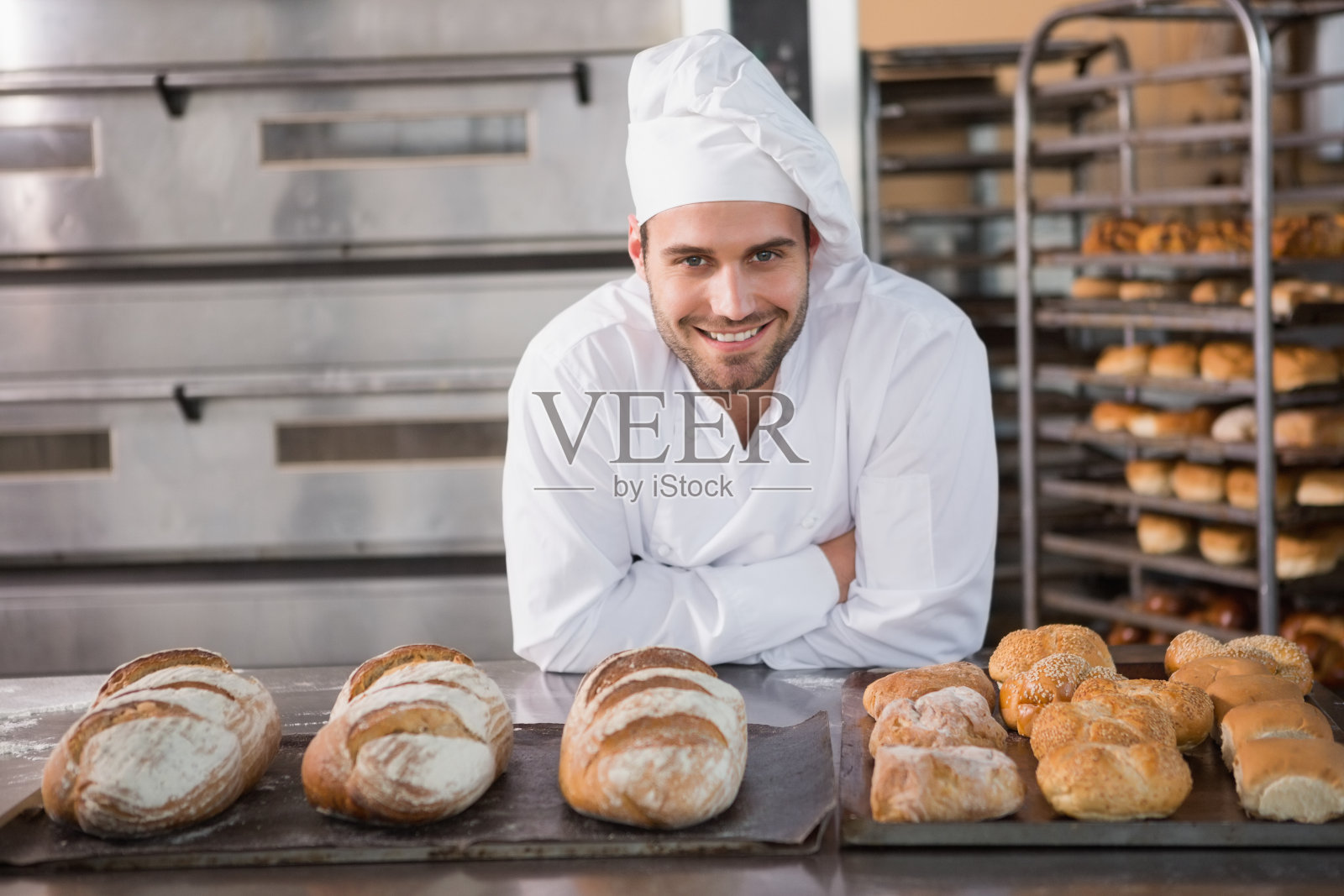 英俊的面包师站在装满面包的托盘旁边照片摄影图片