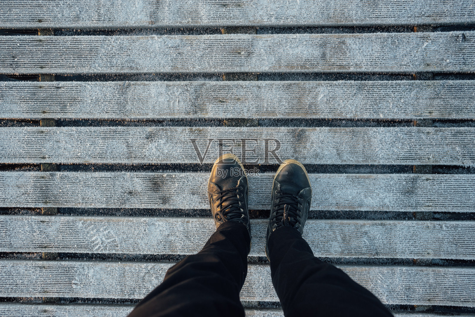 男人的腿穿着靴子放在冰冻的木板上照片摄影图片