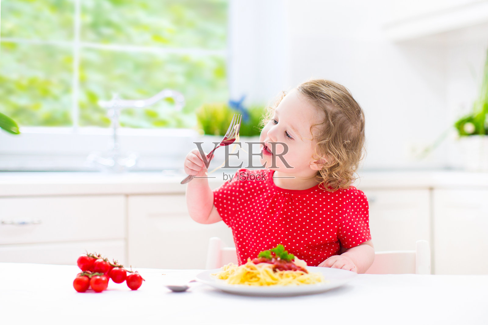 甜美的蹒跚学步的小女孩在白色的厨房里吃意大利面照片摄影图片