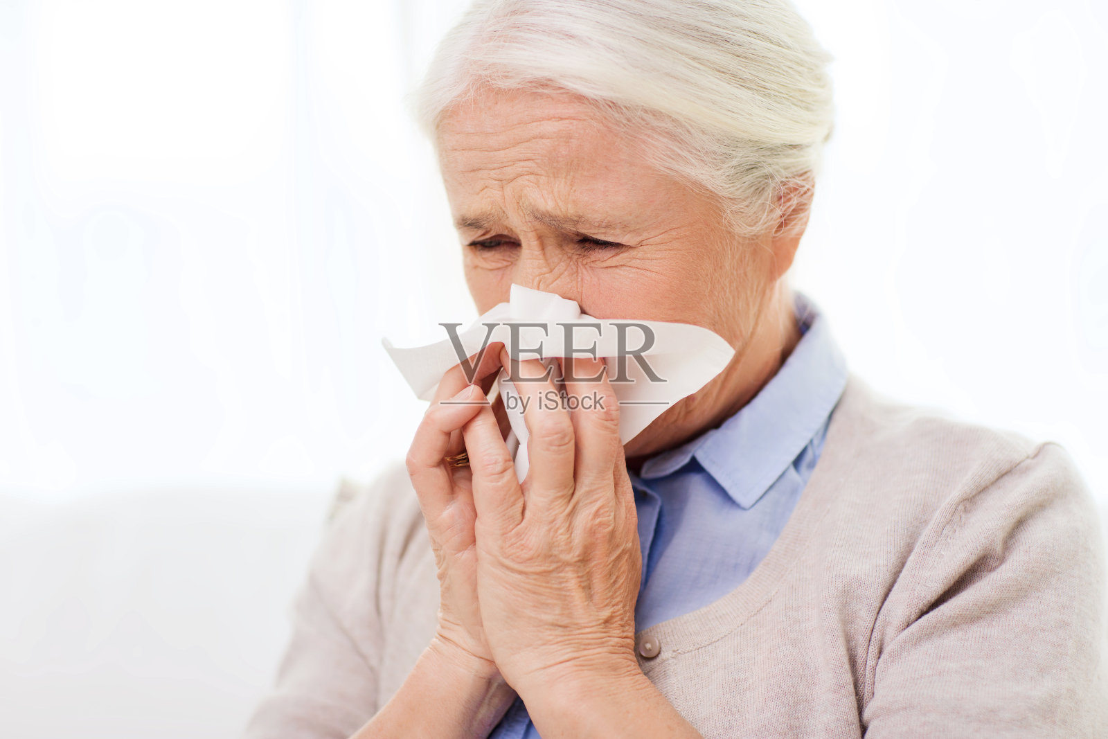 生病的老女人用纸巾擤鼻子照片摄影图片