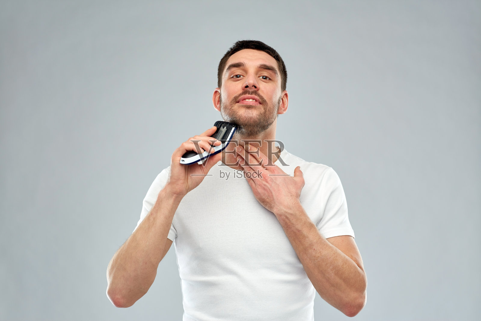 微笑的男人剃胡子用修剪器在灰色照片摄影图片