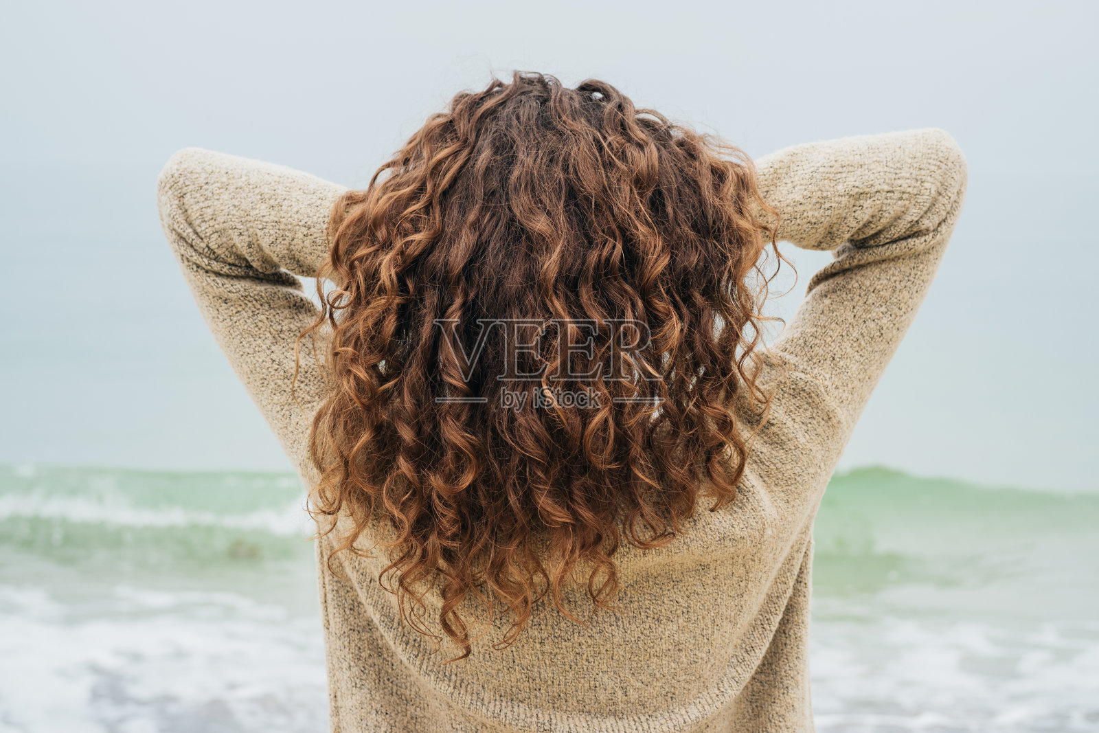 穿着毛衣的黑发卷毛妞在海边照片摄影图片