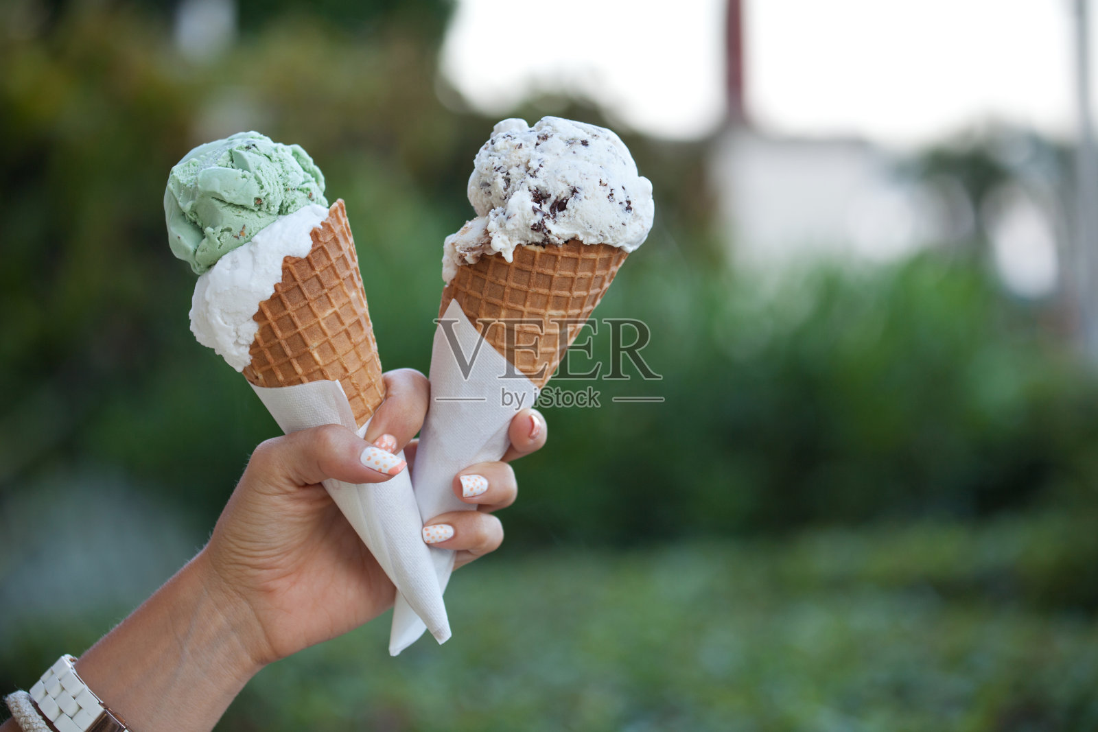 手里拿着两个五颜六色美味的甜筒冰淇淋。照片摄影图片