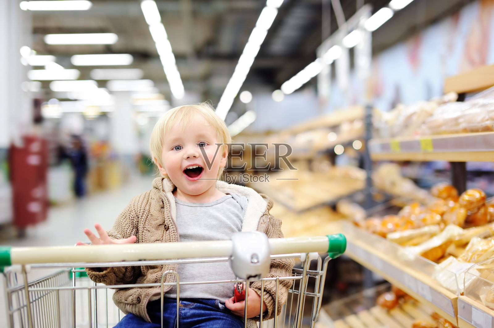 小男孩坐在超市的购物车里照片摄影图片
